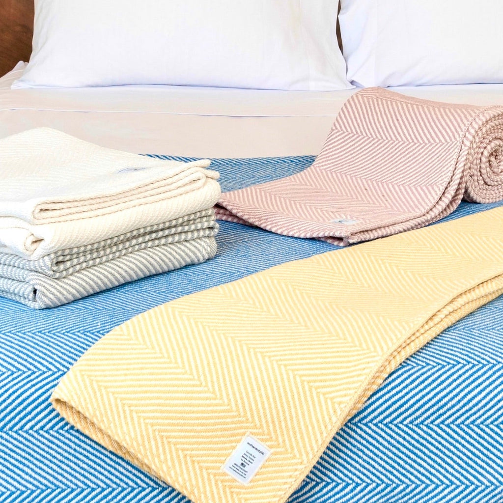 All 5 Authenticity50 Heritage Blankets on a bed; Island Sand, Coastal Blue, Prairie Yellow, Desert Blush & Cascade Gray
