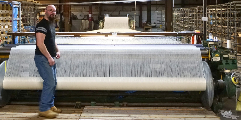 man standing in front of a warp connected to a loom, weaving blankets
